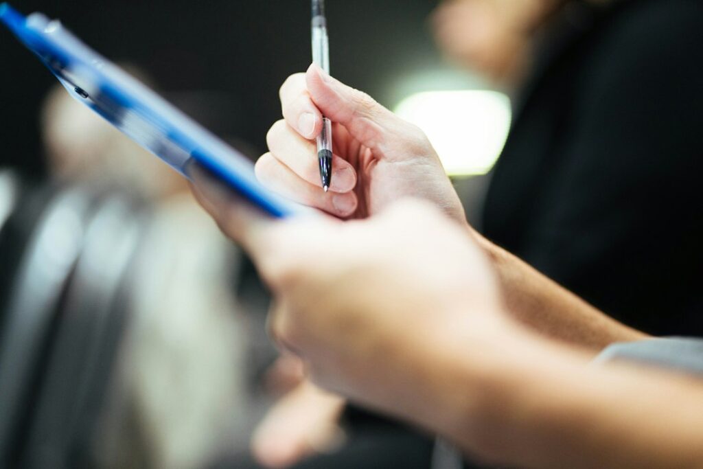 Hand holding a pen over a clipboard, representing an ISO 9001 certification audit